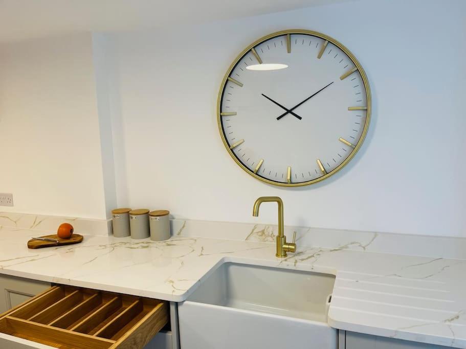 a large clock hanging on a wall above a kitchen sink at Chelston Grange Torquay Near the Beach with Private Garden & Parking in Torquay