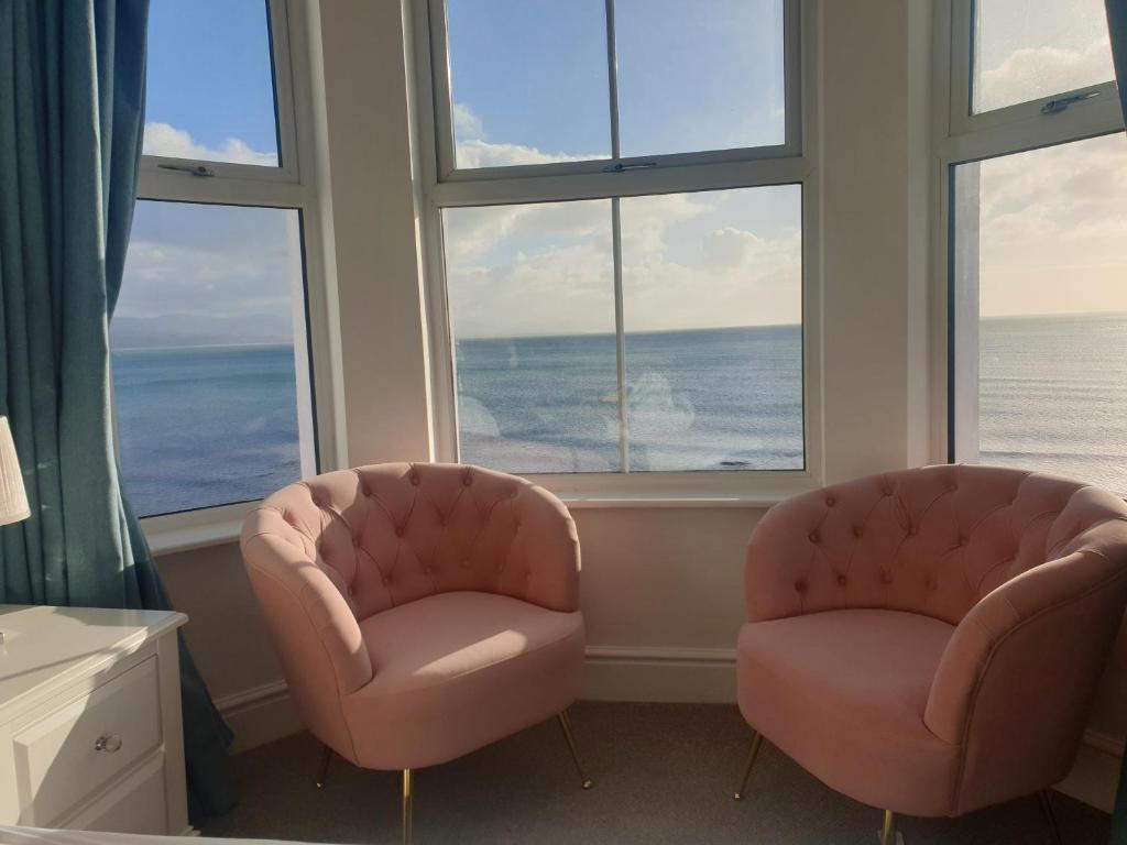 two pink chairs sitting in a room with windows at Glan y Mor, Sleeps 20, 8 Bedrooms, 8 Bathrooms, Seafront, Criccieth in Criccieth