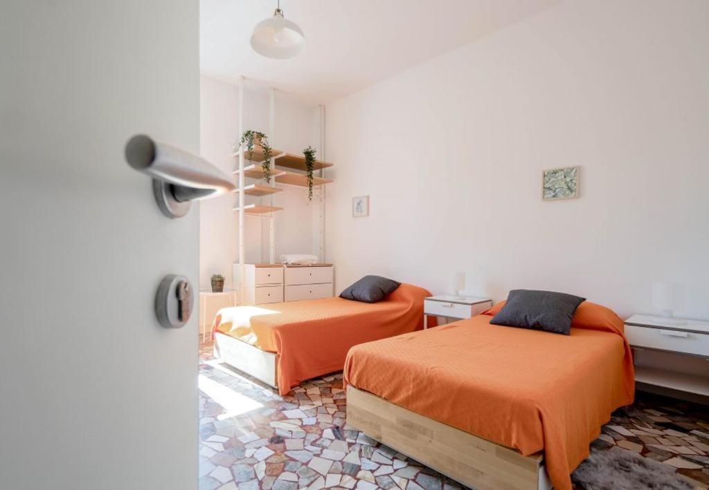 2 Betten in einem weißen Zimmer mit orangefarbener Bettwäsche in der Unterkunft Casadelfalegname 