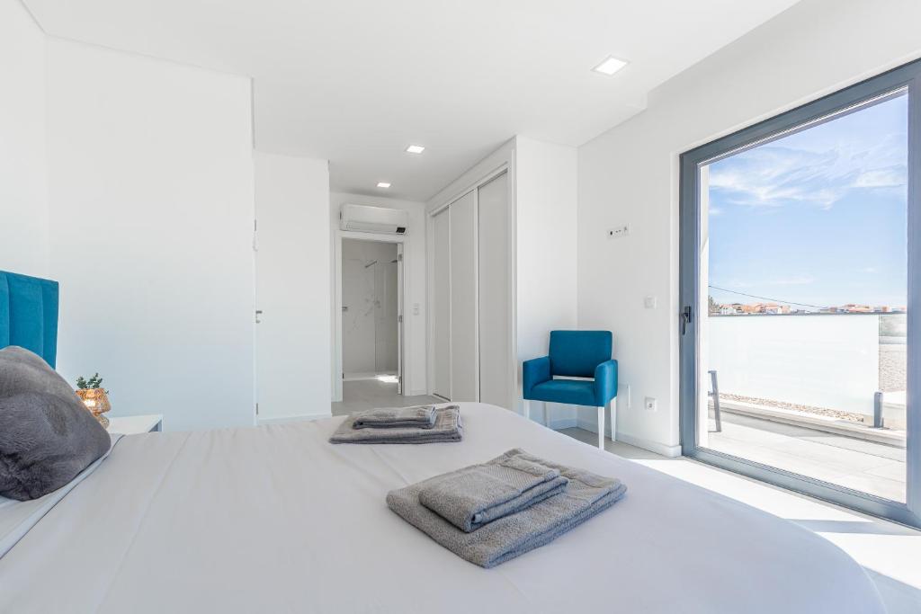a white bedroom with a large bed and a blue chair at Villa Locki in Lourinhã