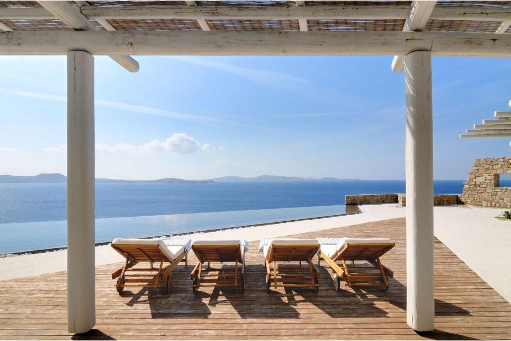 un grupo de sillas y mesas en una terraza con vistas al océano en Luxurious Mykonos Villa 7 Bedrooms Villa Melianthe Private Infinity Pool and Astounding Sunset Sea Views Agios Ioannis, en Dexamenes