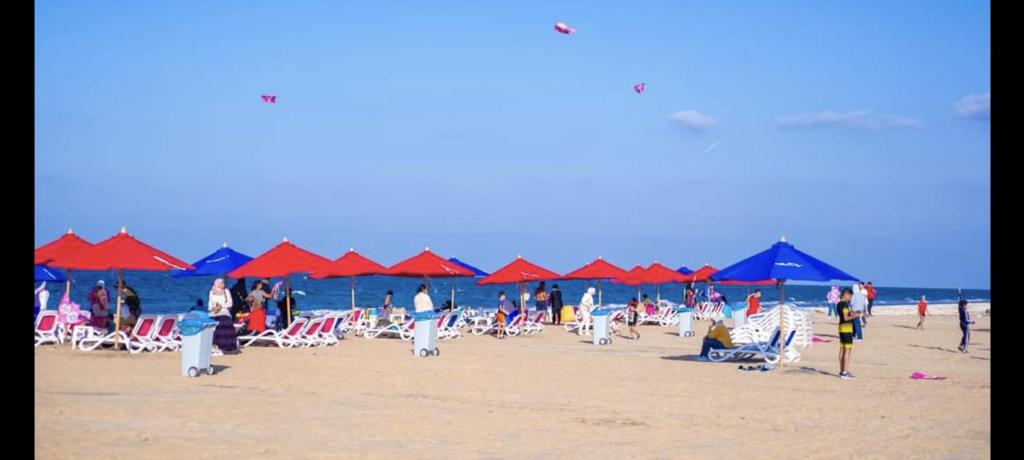 un gruppo di persone su una spiaggia con ombrelloni rossi e blu di Port Said city, Damietta Port Said coastal road num2996 a Port Said