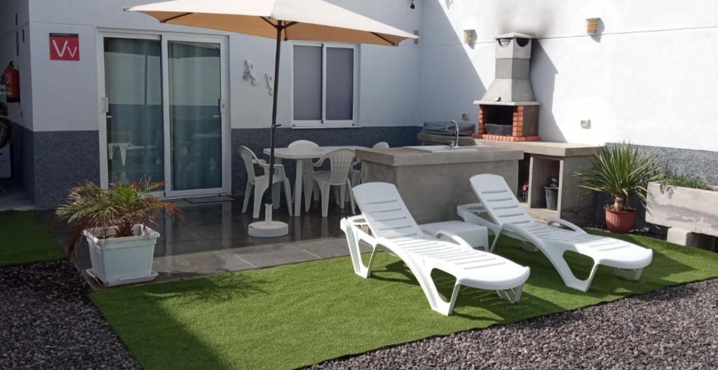 a patio with white chairs and a table with an umbrella at Caleta de Interian Loft Sasy in Los Silos