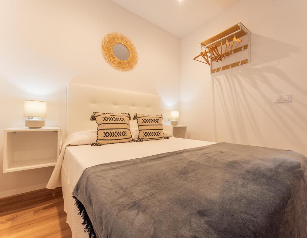 a white bedroom with a bed with two pillows at Apartamentos Turísticos Jardín del Albarregas in Mérida