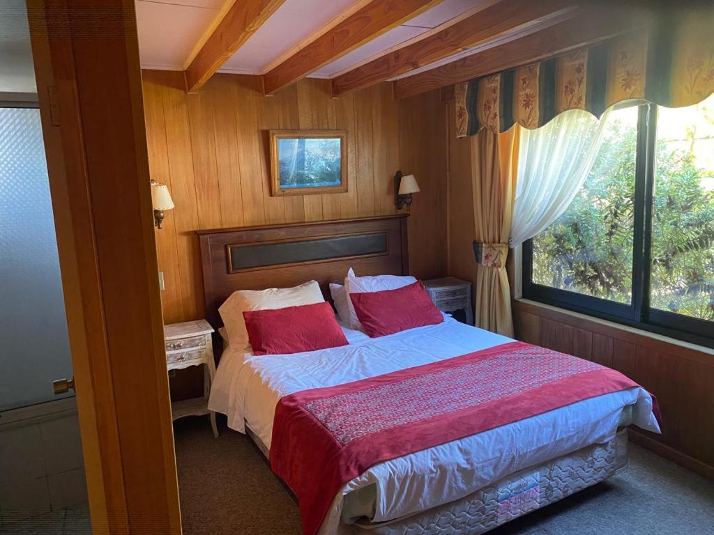 a bedroom with a bed with red pillows and a window at Hostal Buenaventura in Valdivia
