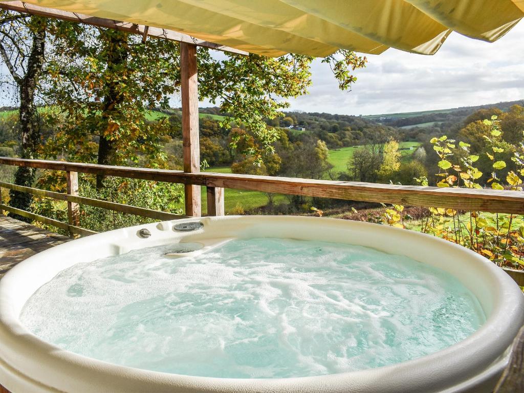 a jacuzzi tub on a balcony with a view at Wampford Woodland Retreat - Kings Cabin in George Nympton