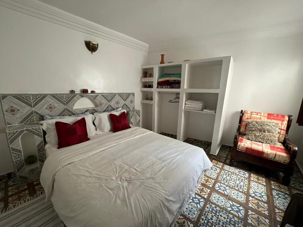 - une chambre dotée d'un lit blanc avec des oreillers rouges et une chaise dans l'établissement Maison Berj, à Oualidia