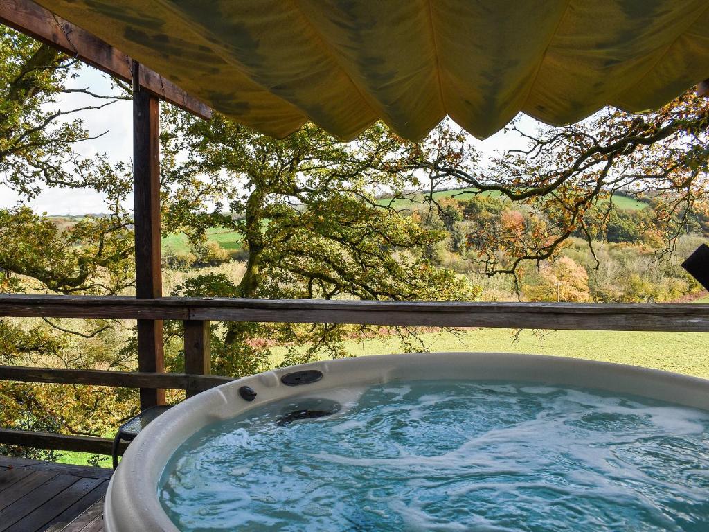 a jacuzzi tub on a porch with a view at Wampford Woodland Retreat - George Cabin in George Nympton