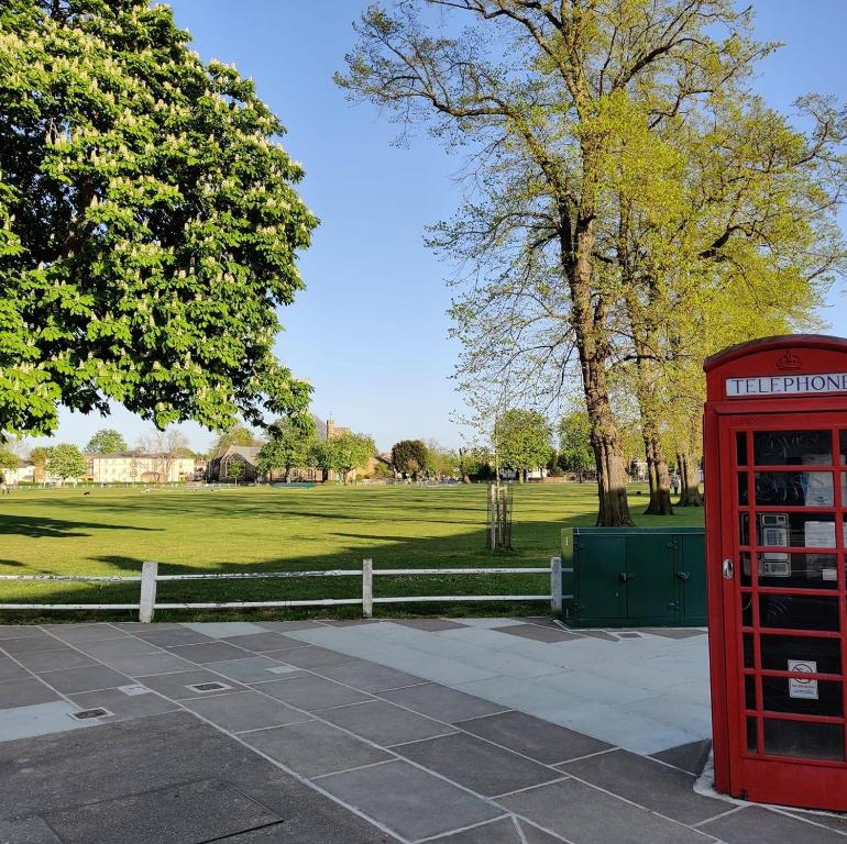 uma cabine telefónica vermelha num parque com um campo em Twickenham Apartments by Charles em Teddington