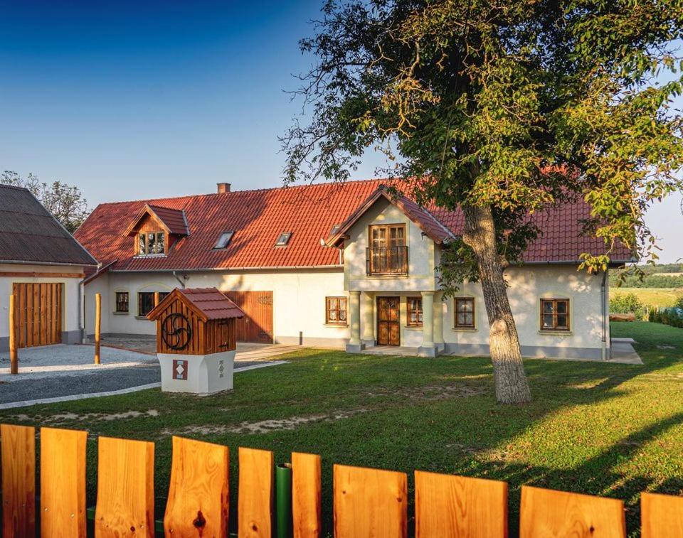 a house with a tree in front of a fence at Nosztalgiavendégház Zalaháshágy in Zalaháshágy