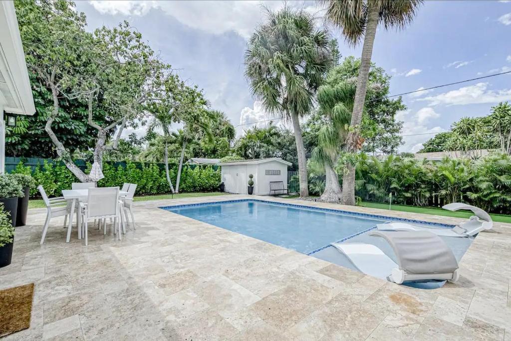 a swimming pool with chairs and a table and trees at Avocado Hideaway in Boynton Beach