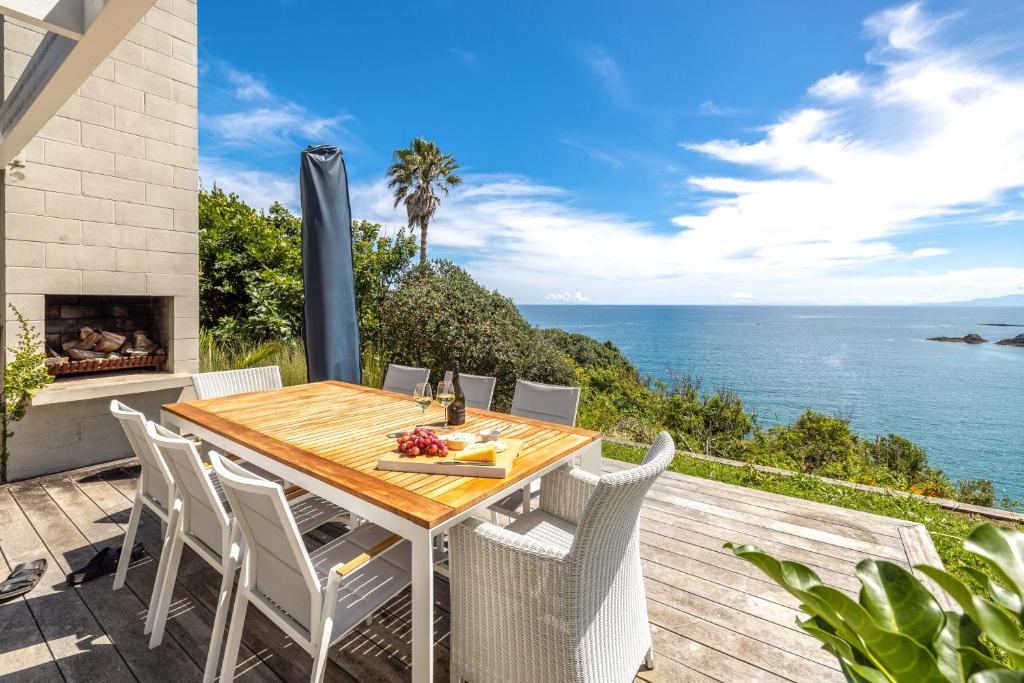 una mesa de madera y sillas en una terraza con vistas al océano en Clifftop Sanctuary en Oneroa