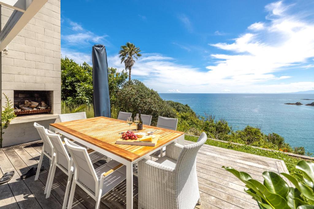 a wooden table and chairs on a deck with the ocean at Clifftop Sanctuary in Oneroa