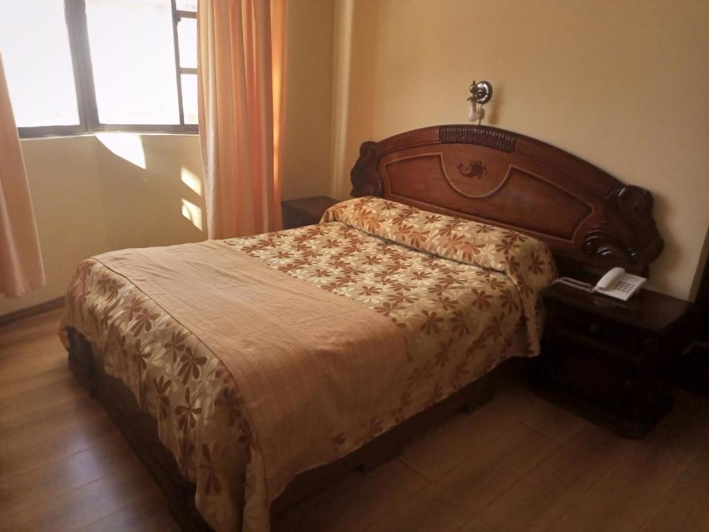 a bedroom with a bed with a wooden headboard and a window at Hotel el LUCERO in Oruro