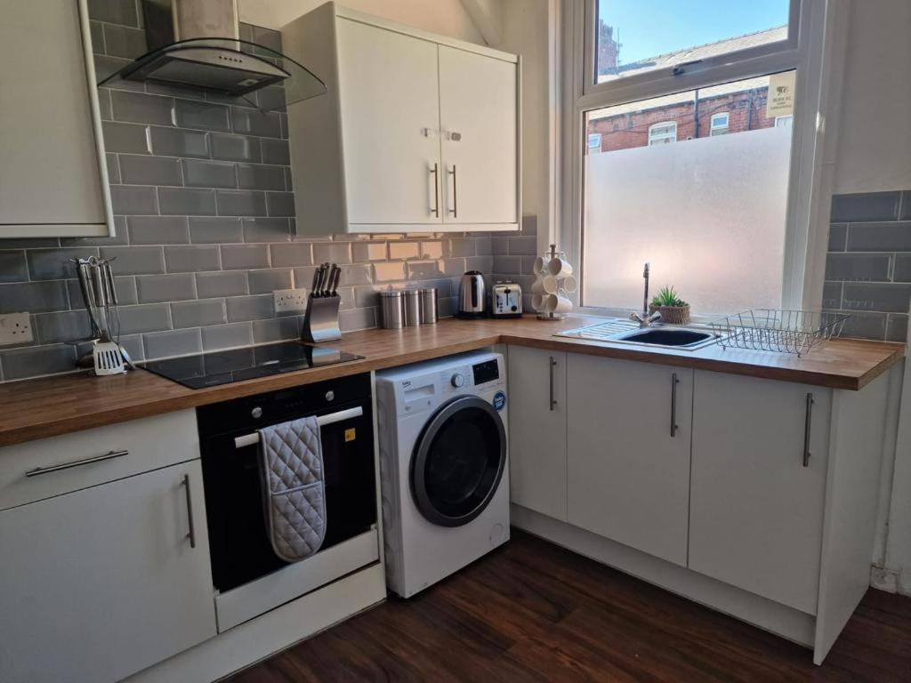 a kitchen with white cabinets and a washer and dryer at Cosy 3 Bedroom House in Beeston, Leeds, LS11 7JP in Beeston