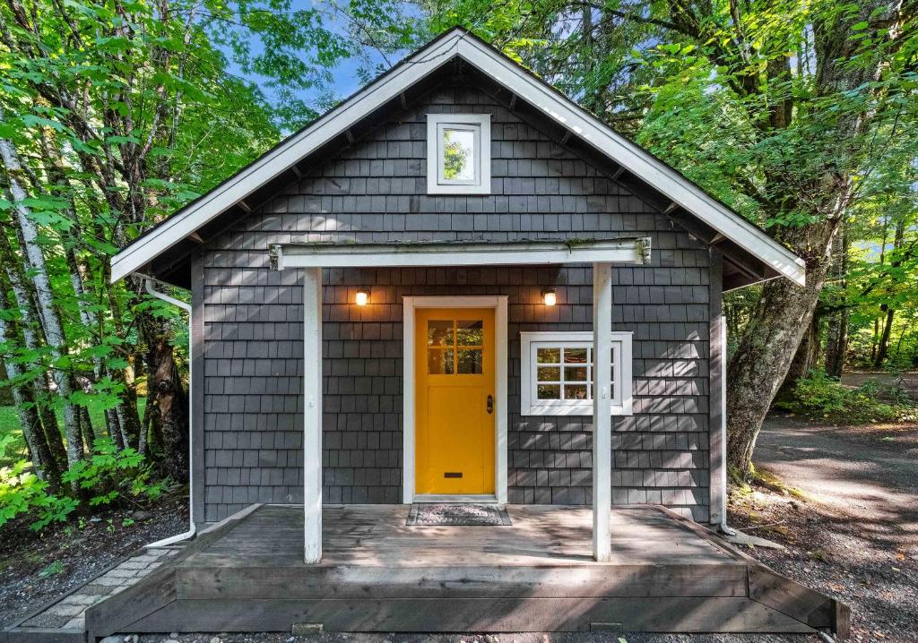 uma pequena casa com uma porta amarela na floresta em Sunwolf Riverside Cabins em Brackendale