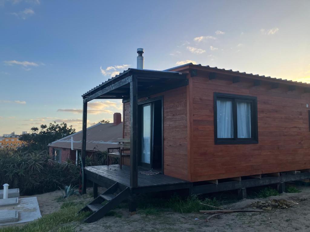 a small wooden house with a porch on a field at El banzai in Punta Del Diablo