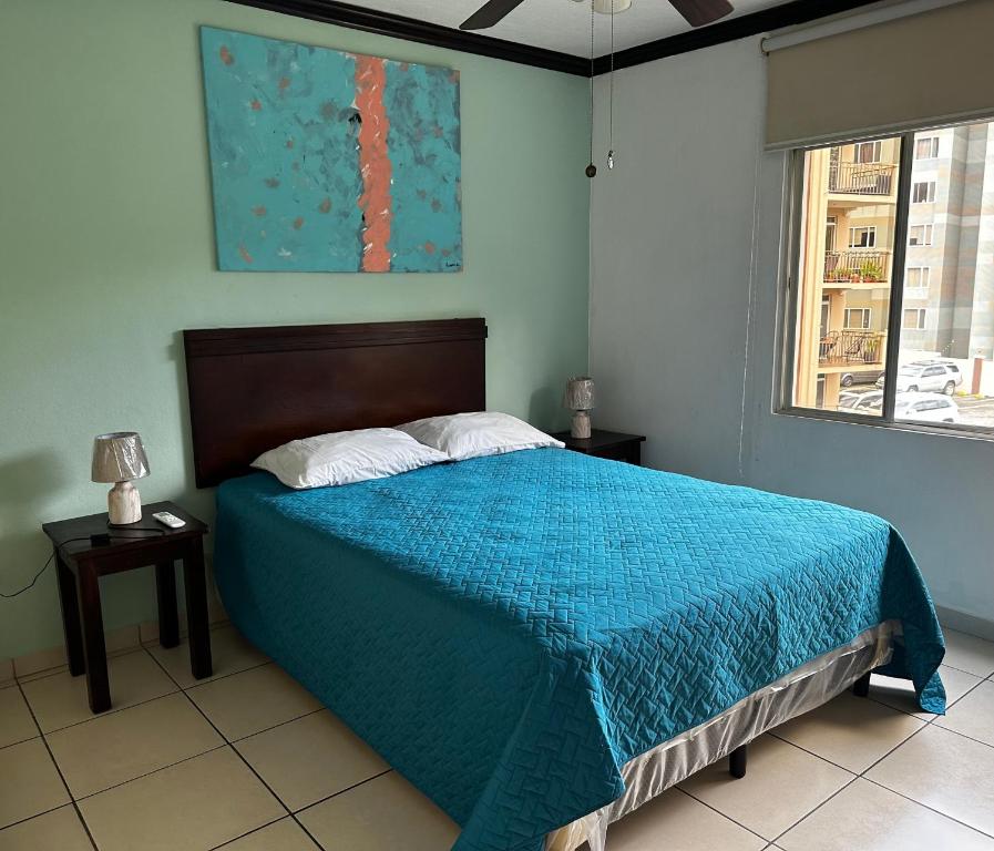 a bedroom with a bed with a blue blanket and a window at MonBlanc in San Salvador
