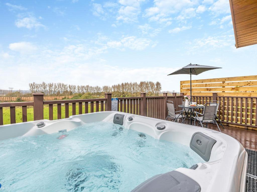 a hot tub on a deck with a table and an umbrella at Billy Goat Lodge in Crossway Green