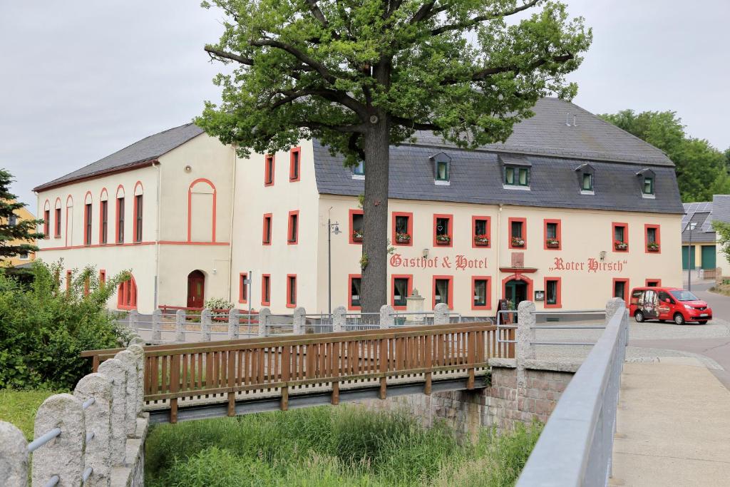ein großes weißes Gebäude mit einem Baum davor in der Unterkunft Gasthof und Hotel Roter Hirsch in Claußnitz