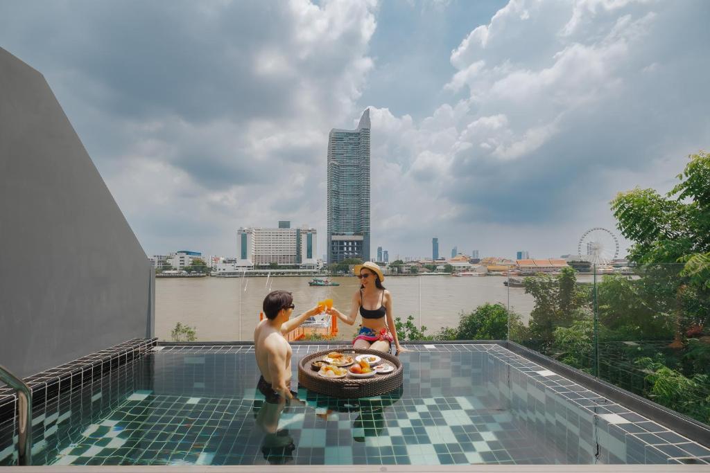 A rooftop-style pool frames a wide river and Bangkok skyline.