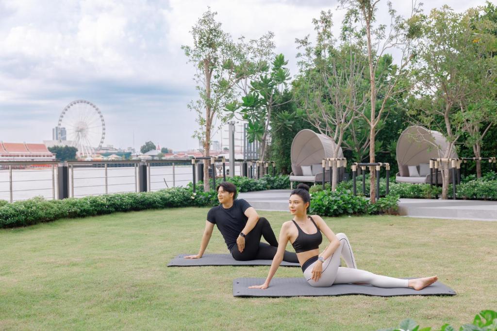 Two people practise yoga on mats across a riverside lawn.