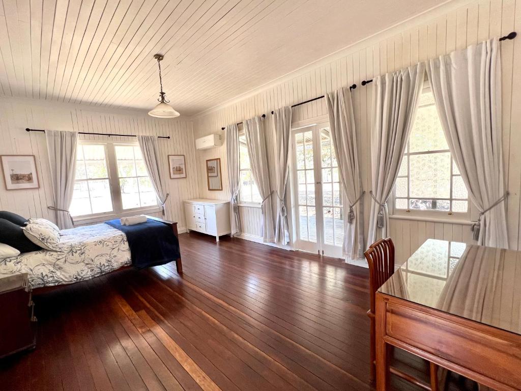 a bedroom with a bed and wooden floors and windows at The Cottage Farm Stay - Grandchester in Grandchester