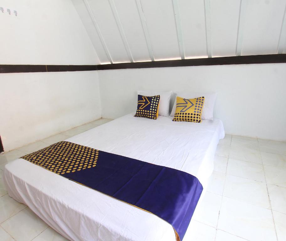 a white room with a bed with blue and yellow pillows at OYO Life 93154 White Kos Jenggala in Tanjung