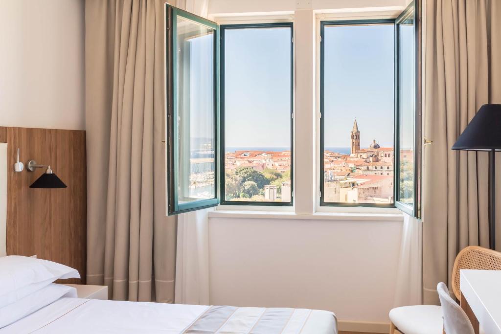 een slaapkamer met een raam met uitzicht op de stad bij Hotel Catalunya in Alghero