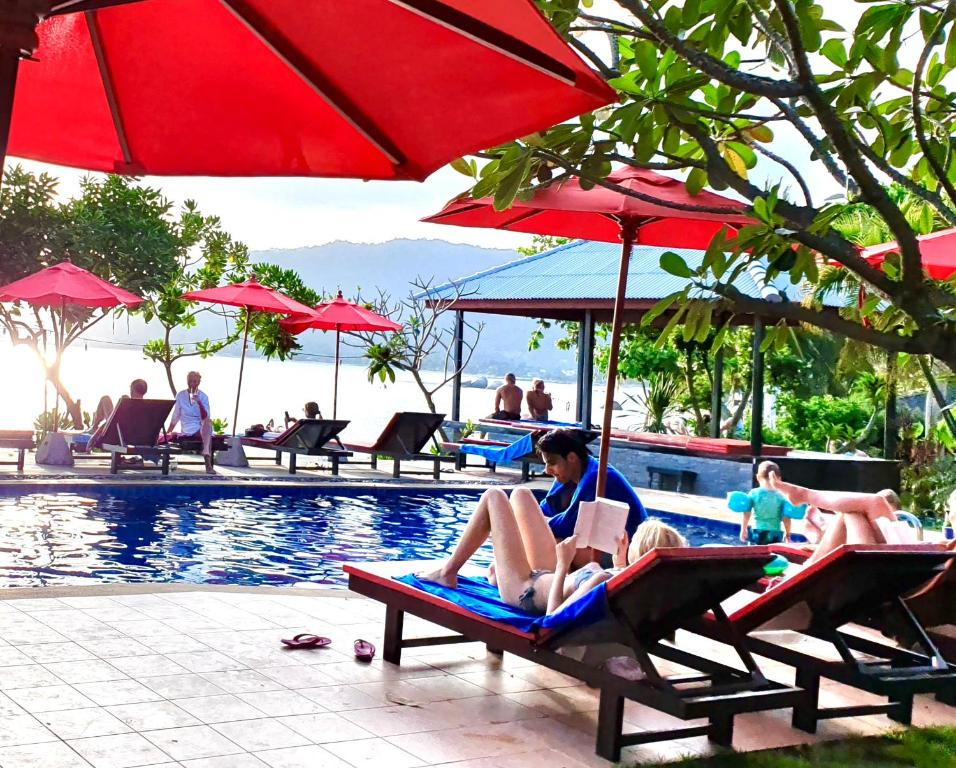 a group of people sitting on lounge chairs next to a pool at Cinnamon Beach Villas in Lamai