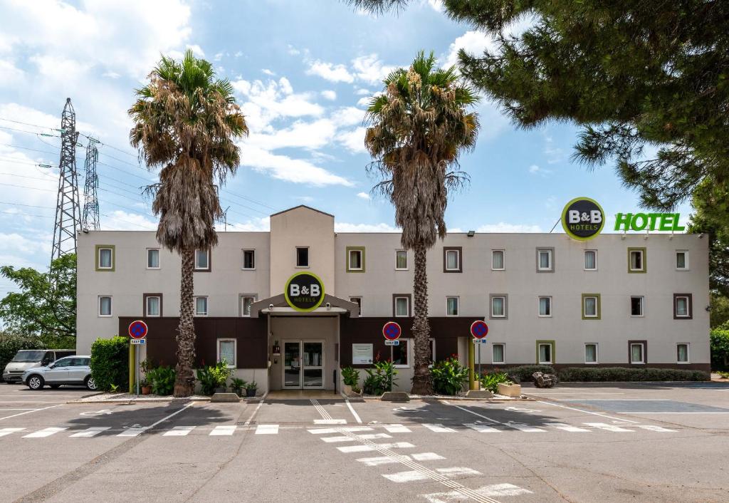 un hôtel avec des palmiers devant lui dans l'établissement B&B HOTEL Montpellier 1, à Saint-Jean-de-Védas
