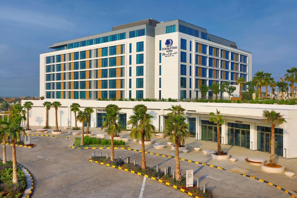 Doubletree By Hilton Abu Dhabi Yas Island Residences في أبوظبي: مبنى كبير أمامه أشجار نخيل