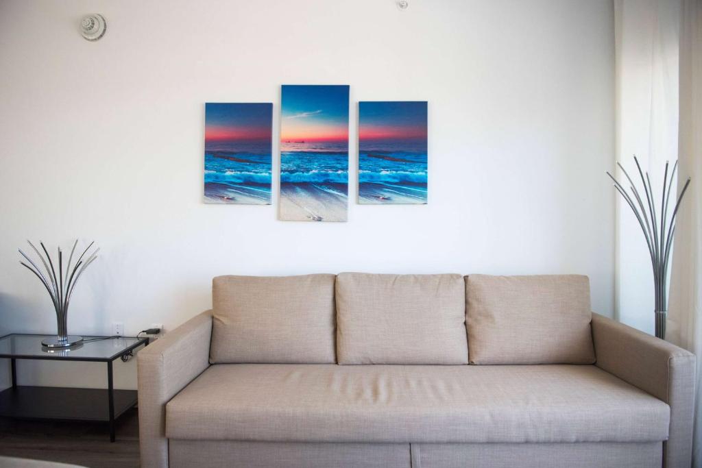 a couch in a living room with four paintings of the ocean at 12th & Ocean by LuxUrban, Trademark Collection by Wyndham in Miami Beach