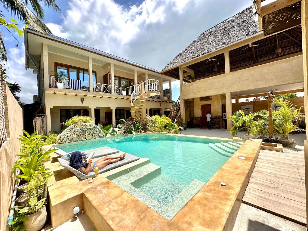 a woman laying on a chair in a swimming pool next to a house at Chikachika Beach B&B in Nungwi