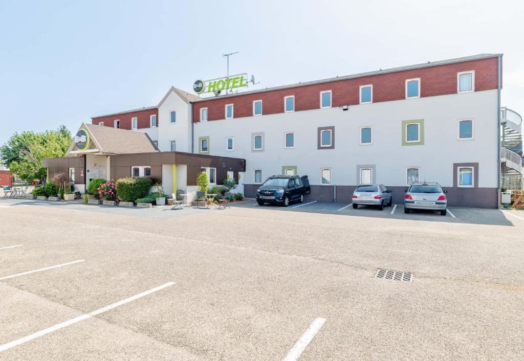 a large building with cars parked in a parking lot at B&B HOTEL Lyon Saint-Bonnet Mi-Plaine in Saint-Bonnet-de-Mure