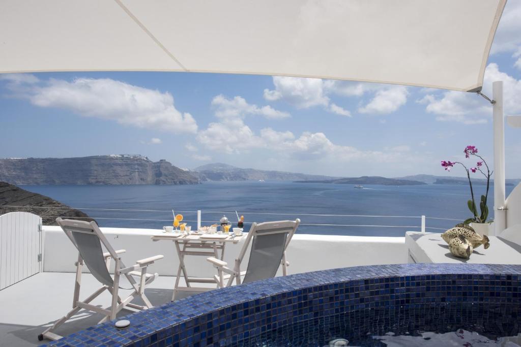 balcón con mesa, sillas y vistas al océano en Ambition Suites en Oia