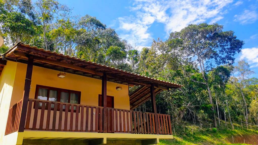 a yellow house with a balcony and trees in the background at Chalé Céu de Minas in Visconde De Maua