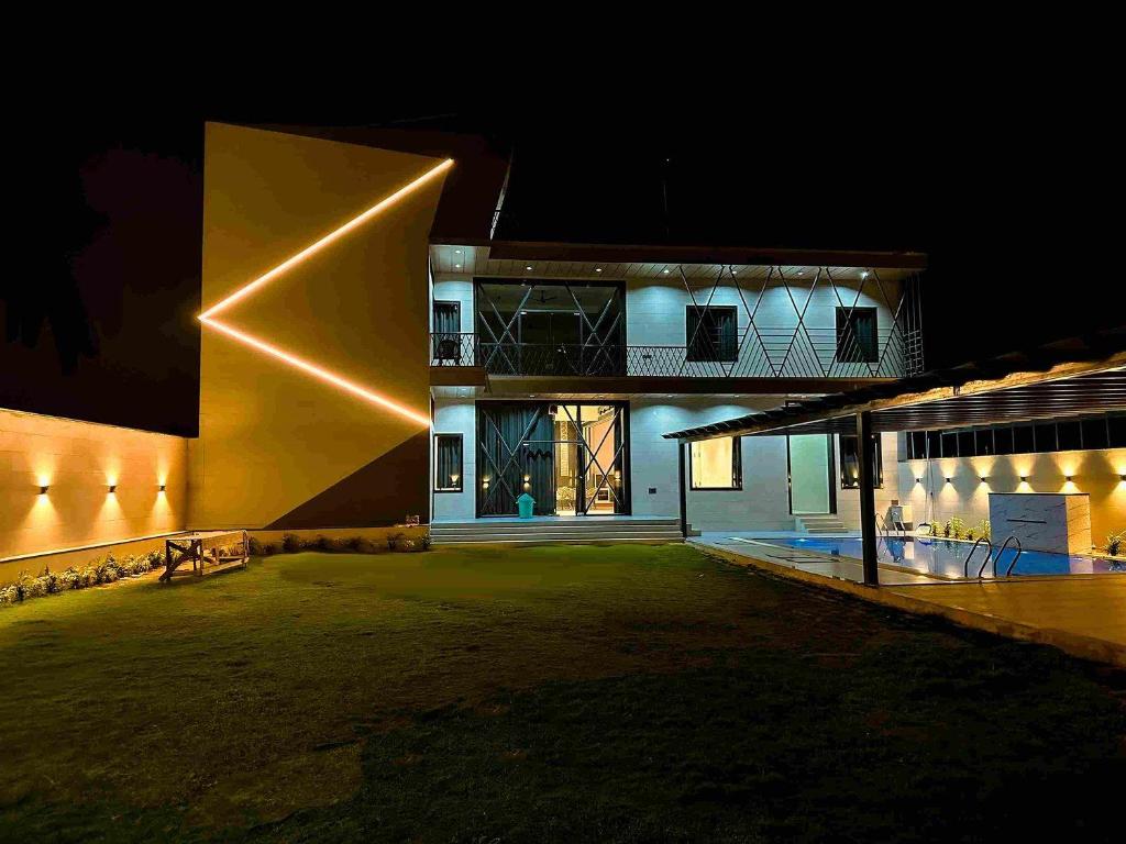 a house lit up at night with a large building at Grazio outhouse, A Contemporary designed 4bhk farm with swimming pool, massive living areas, bar. in Begās