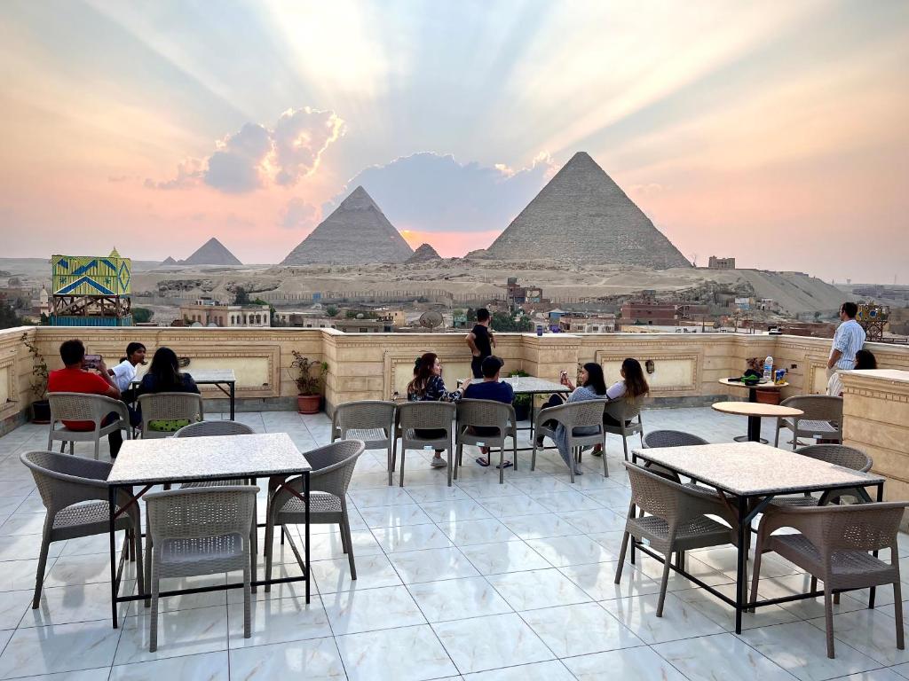 pessoas sentadas em mesas num telhado com pirâmides ao fundo em Moses Pyramids Inn no Cairo