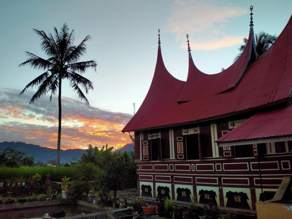 un bâtiment avec un toit rouge à côté d'un palmier dans l'établissement Rumah Gadang Homstay, à Baso
