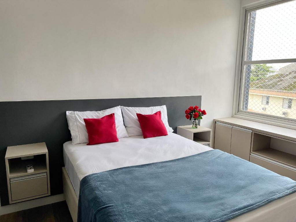 Schlafzimmer mit einem Bett mit roten Kissen und einem Fenster in der Unterkunft Moderno Vista Mar - AR | Piscina | Vaga Garagem in São Vicente