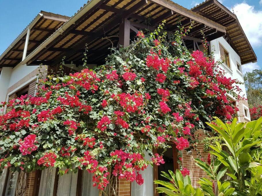 Ein Haufen roter Blumen hängt von einem Gebäude in der Unterkunft Casa em condomínio fechado na Serra Guaramiranga in Pernambuquinho