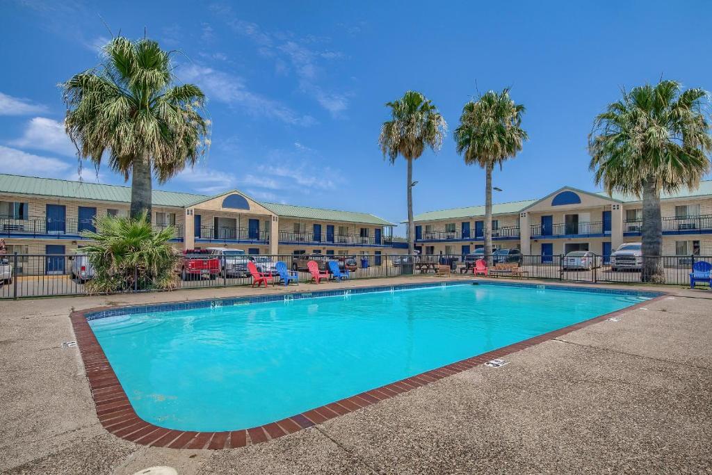 a swimming pool in front of a building with palm trees at Welcome Inn in Eagle Pass