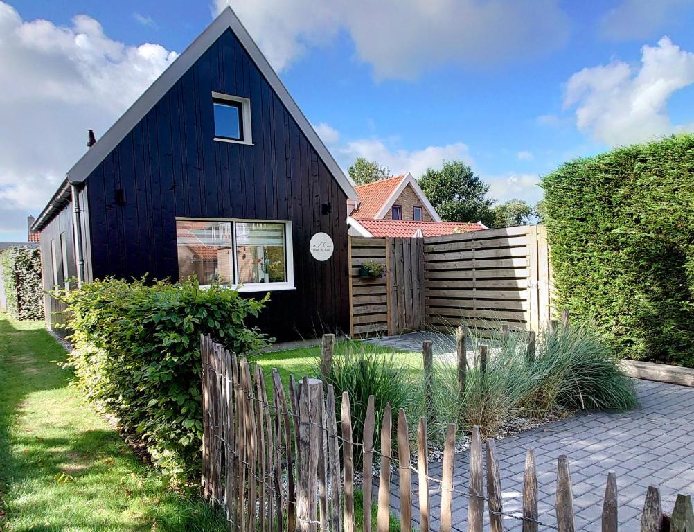 a black house with a wooden fence in front of it at Naar de kust in Hollum