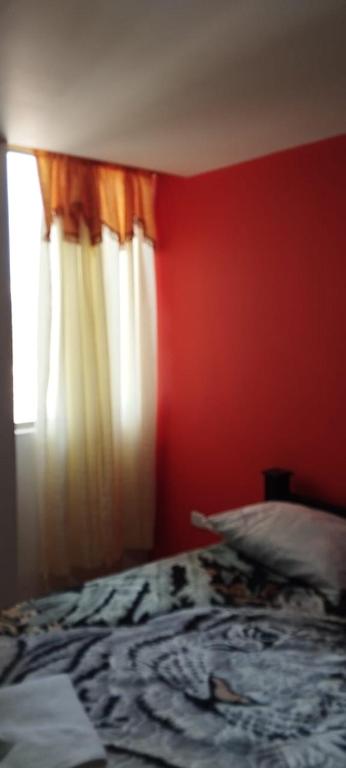 a bedroom with a bed with a red wall and a window at Ipiales Puerta de Oro Alborada in Ipiales