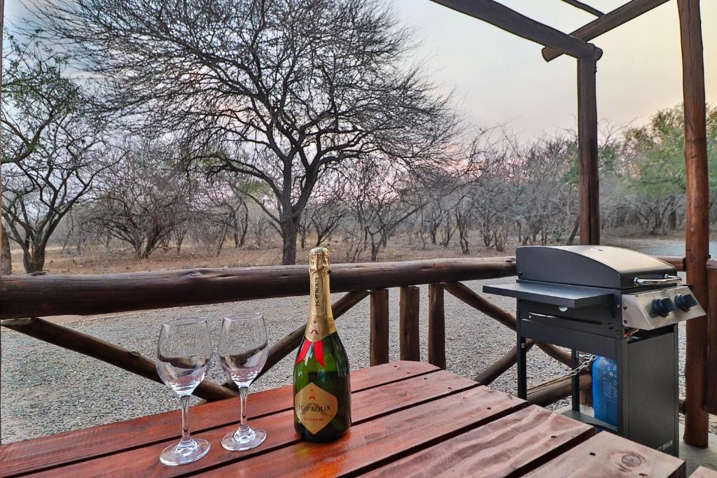 Una botella de champán sobre una mesa de madera con copas de vino. en Lion Den, en Marloth Park