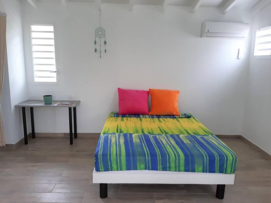 a bedroom with a bed with colorful sheets and a table at Le Gîte Petit colibri in Sainte-Rose