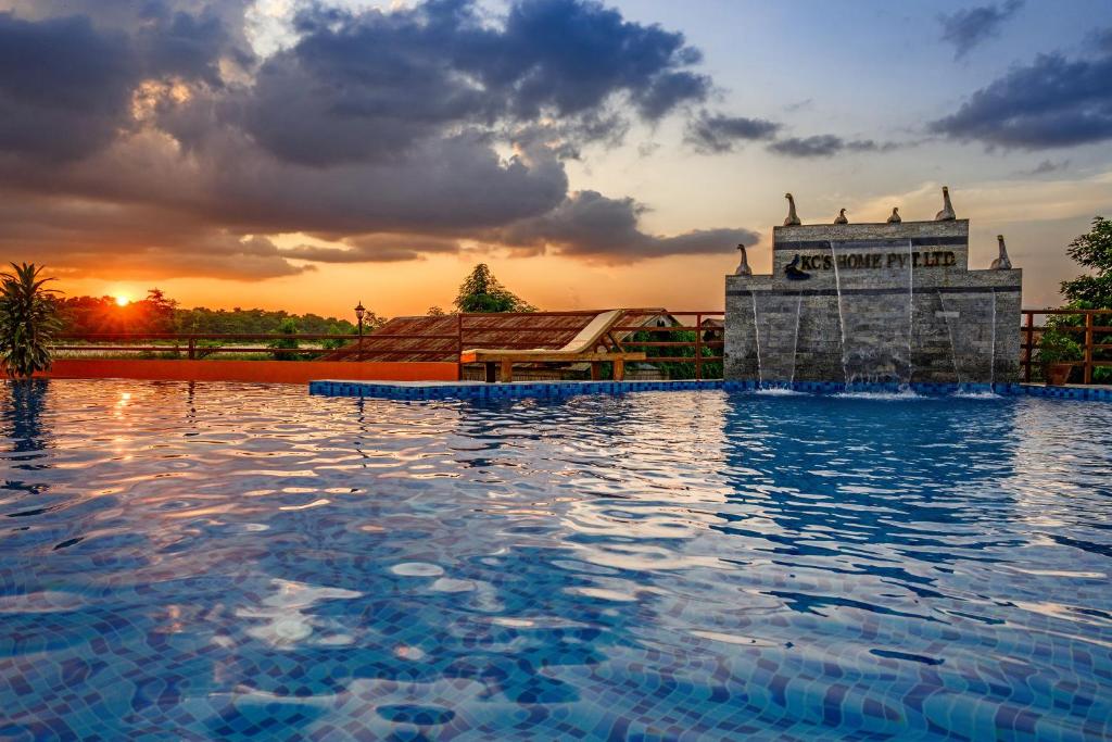 a large swimming pool with a water fountain in front of a sunset at KC's Home in Sauraha