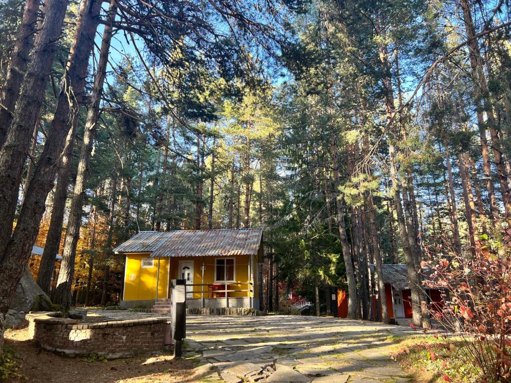 a small yellow house in the middle of a forest at Почивна база Пиринпласт in Gotse Delchev