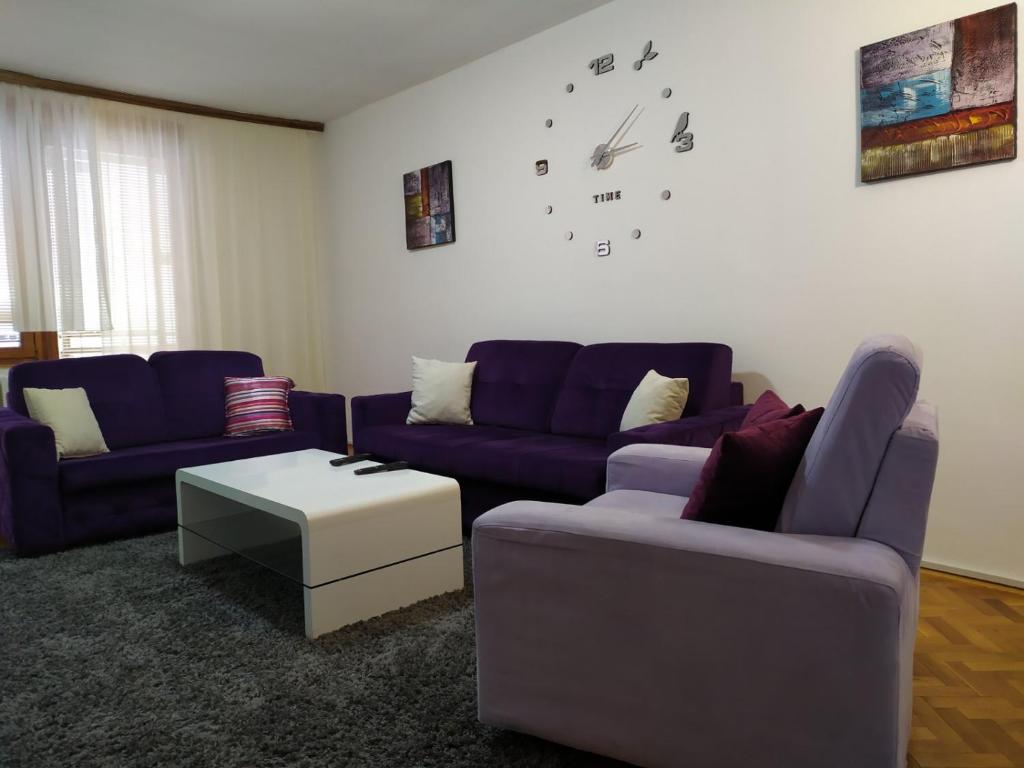 サラエボにあるHanaDi Apartmentの紫色のソファ2台と壁掛け時計付きのリビングルーム
